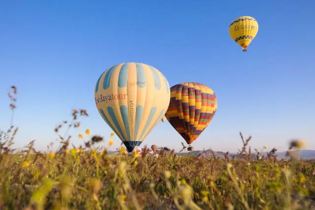 Three Air Balloons Over A Field With A Blue Sky Background